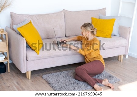 Side view. Beautiful woman checks email online, uses modern laptop, works remotely, uses Wi-Fi. Nice woman smiling sitting on the floor near the sofa at home on a white background. Copy space