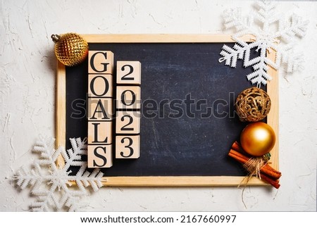 Goals 2023 black writing board, wooden cubes with inscription. Copy space in the center. Christmas balls and snowflakes frame.