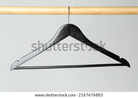 Black clothes hanger on wooden rail against light grey background