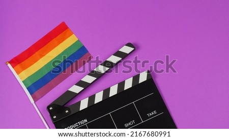 A rainbow flag and black clapperboard on purple background. LGBT CONCEPT.	

