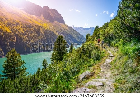 Alpine track and two hikers at mountain lake Royalty-Free Stock Photo #2167683359