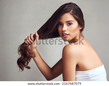 My hair regime has made my hair stronger. Studio shot of a young beautiful woman with long gorgeous hair posing against a grey background. Royalty-Free Stock Photo #2167687079