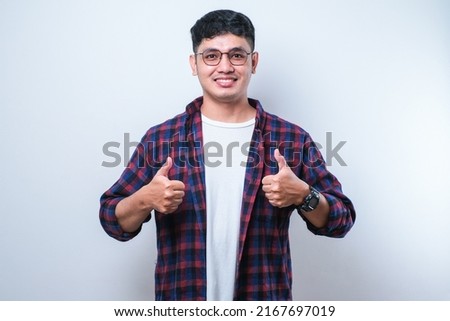 Young handsome man wearing casual shirt over white background approving doing positive gesture with hand, thumbs up smiling and happy for success. Winner gesture. Royalty-Free Stock Photo #2167697019