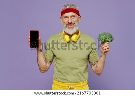 Fun elderly gray-haired man 50s years old in headband khaki t-shirt hold mobile cell phone with blank screen workspace area broccoli isolated on plain pastel light purple background studio portrait