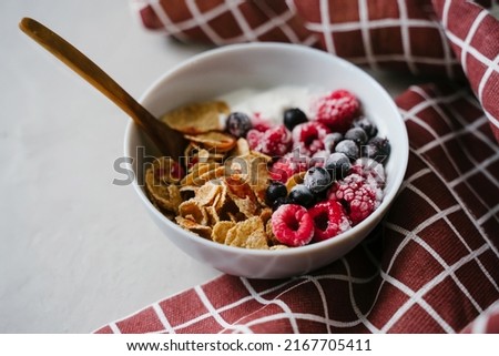 Healthy breakfast with yoghurt, berries and cereals. Wooden spoon. Multi-lacquered cereals for breakfast. Red plaid towel.