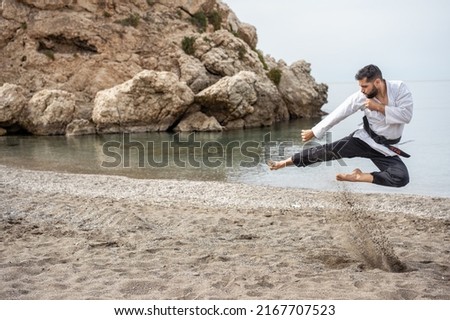 martial arts expert in a kimono performing a flying kick on the beach and whose belt reads in Japanese "bushido". Royalty-Free Stock Photo #2167707523
