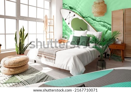 Stylish interior of bedroom with boards for sup surfing and wall with printed clear water