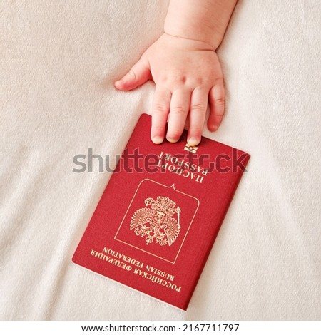 Translation: Russian Federation Passport. Hand baby toddler boy is holding a Russian passport. A child with a document confirming the identity of a citizen of Russia, close-up Royalty-Free Stock Photo #2167711797