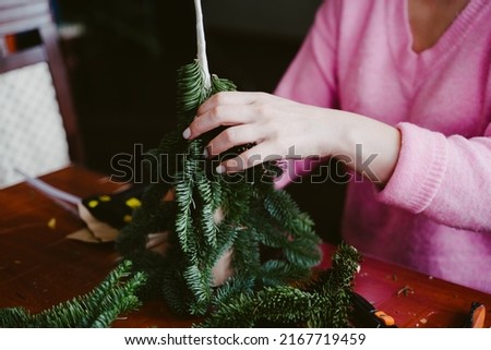 A girl in a pink sweater cuts pieces of floral wire. The girl makes a craft from a natural branch of nobilis. New Year's Eve master class on creating decorations from natural nobilis.