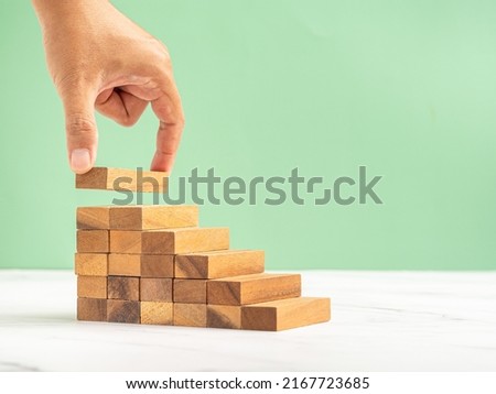 Close-up of hand holding a wooden block arranging to stack for development as step stair on a marble floor over a green background. Business growth, and success plan concept