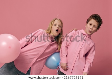 little school-age children have fun standing on a pink background making funny faces and holding pink and blue balloons in their hands