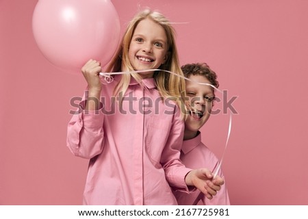 happy children a boy and a girl of school age indulge in stya on a pink background, the girl holds a pink balloon in her hand, and the boy hides behind her