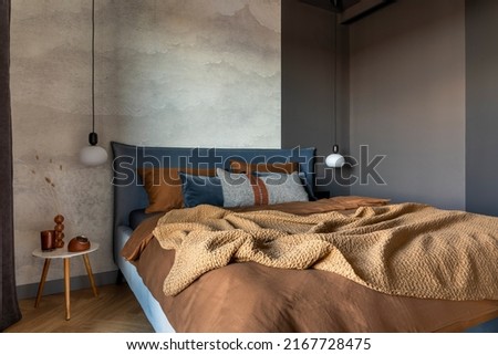 Stylish composition of modern bedroom interior. Bed, creative lamp and elegant personal accessories. Concrete wall. Brown sheeets. Minimalistic masculine concept. Template. Royalty-Free Stock Photo #2167728475