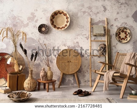 The stylish ethnic composition at living room interior with design brown armchair, colorful baskets, rattan sideboard and elegant personal accessories. Grey concrete wall. Cozy apartment. Home decor.  Royalty-Free Stock Photo #2167728481