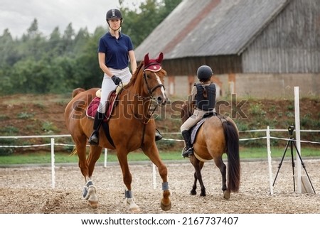 Equestrian sport -young girl rides on horse and little girl rides on pony in during training. Royalty-Free Stock Photo #2167737407