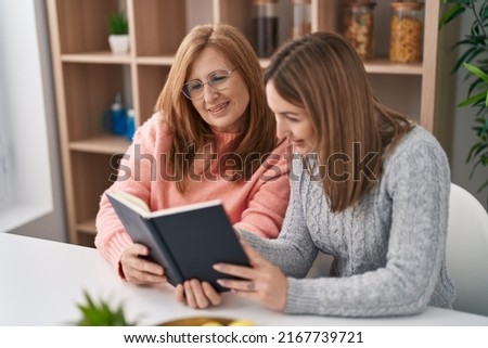 Mother and daughter reading book sitting on desk at home
