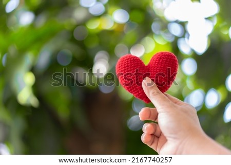 Hand holding red yarn heart shape with natural beauty background in sunny day.
