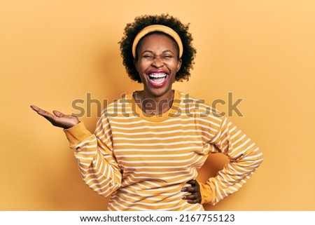 Young african american woman presenting with open palms, holding something smiling and laughing hard out loud because funny crazy joke. 