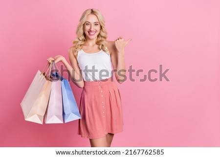 Portrait of attractive cheerful wavy-haired girl buying clothes showing ad copy space isolated over pink pastel color background