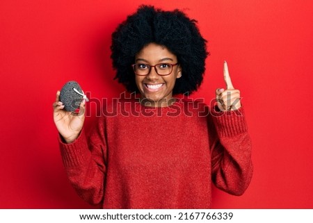 Young african american woman holding pumice stone smiling with an idea or question pointing finger with happy face, number one 