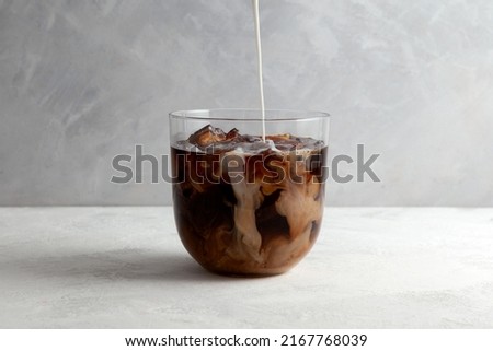 Cold iced coffee with Almond milk. Refreshing drink is poured into a clear glass. Grey background, selective focus.