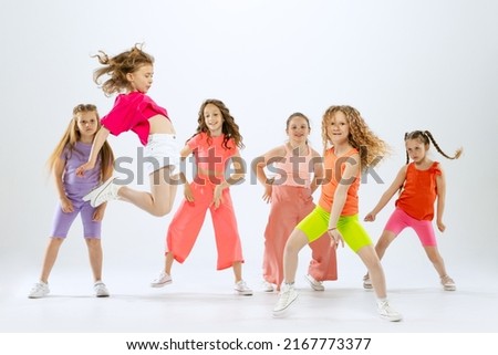 Joy, fun and happiness. Portrait of happy, active little girls, happy kids in bright colorful clothes dancing isolated on white studio background. Concept of music, fashion, art, childhood, hobby.