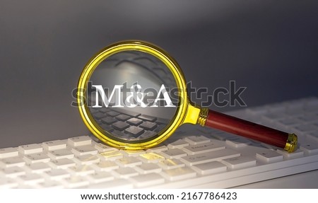 M and A text on a magnifier on a keyboard, business concept
