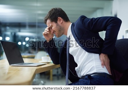 Time for some lumbar support. Shot of a businessman wincing in pain and holding his lower back while sitting at a desk in an office. Royalty-Free Stock Photo #2167788837