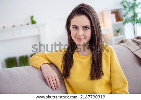 Photo of gorgeous calm person sitting couch look camera enjoy spend free time house indoors