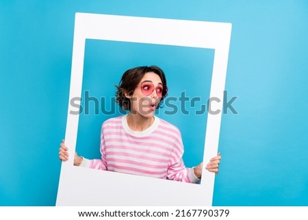 Photo of impressed astonished lady look empty space hold white picture frame isolated on blue color background