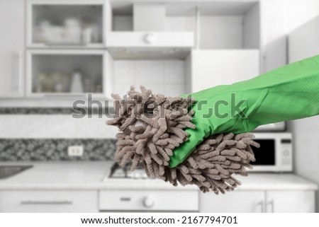 Close-up view of woman's hand in a rubber protective glove with the rag and the kitchen on the background. Cleaning concept.