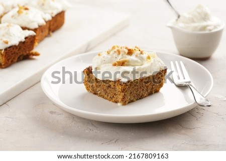 Homemade pastry carrot-walnut cake with grounded almonds and hazelnuts and white cream cheese top layer on white plate
