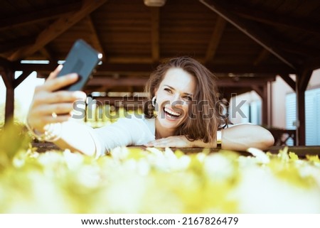 happy stylish middle aged woman in white shirt answering incoming video call on a smartphone on the ranch.