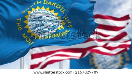 The South Dakota state flag waving along with the national flag of the United States of America. South Dakota is a U.S. state in the North Central region of the United States