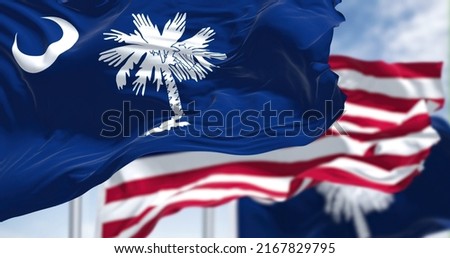 The South Carolina state flag waving along with the national flag of the United States of America. South Carolina is a state in the coastal Southeastern region of the United States