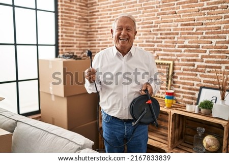 Senior man with grey hair holding extension plug smiling and laughing hard out loud because funny crazy joke. 