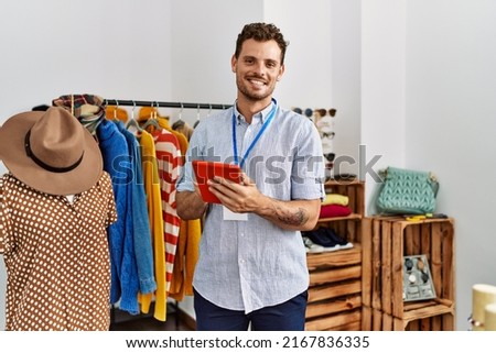 Young hispanic shopkeeper man smiling happy using touchpad working at clothing store. Royalty-Free Stock Photo #2167836335