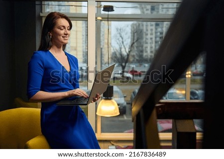 Beautiful successful Caucasian woman- interior designer, businesswoman, sales manager sitting in a yellow nouveau art chair with a laptop in her hands. Stylish interior design. Remote and online work