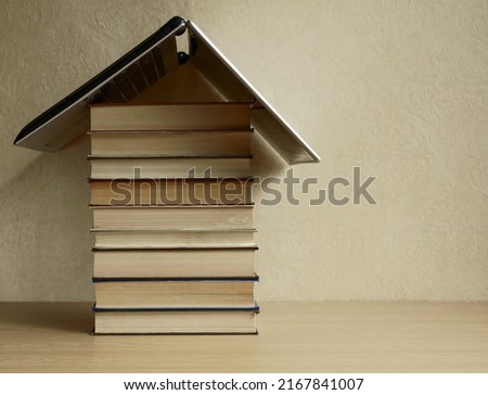 gray Laptop as a roof standing on stack of  books. wooden table. wallpaper background. back to school idea. House, university, college sign, symbol. 
