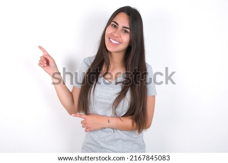 young caucasian woman wearing grey t-shirt over white background indicating finger empty space showing best low prices, looking at the camera