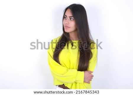 Pleased young caucasian woman wearing yellow sweater over white background keeps hands crossed over chest looks happily aside