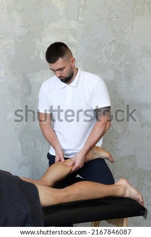 Masseur does legs massage in spa center on gray concrete background. Massage of myofascial trigger points on back of male client to release tension. Rehabilitation, sport therapy medicine.  Royalty-Free Stock Photo #2167846087