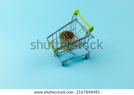 Gold bitcoin coins in metal trolley for groceries from the supermarket on blue background, business, money and finance 