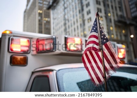 Close-up of American flag against red flasher light of siren of ambulance car. Themes emergency, rescue and help. 
 Royalty-Free Stock Photo #2167849395