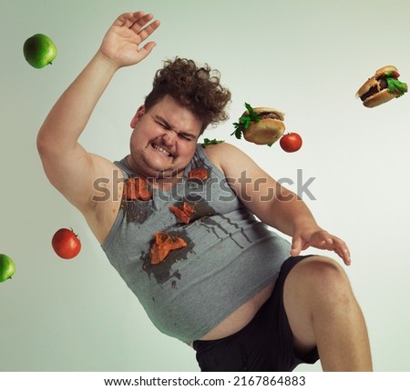Dodge temptation - stick to your diet. Shot of an overweight man dodging food being thrown at him. Royalty-Free Stock Photo #2167864883