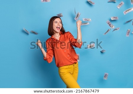Photo of young excited girl rejoice success luck fists hands rich triumph fly cash look empty space isolated over blue color background