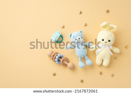 Baby accessories concept. Top view photo of knitted bunny and teddy-bear toys wooden rattle blue pacifier and gold stars on isolated pastel beige background with copyspace