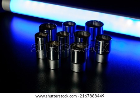 Socket wrench heads made of chrome vanadium on the dark background in a neon blue light. LED tube is giving back light behind the composition. 