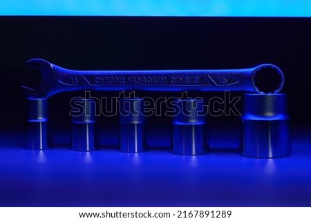 Spanner for 16mm is standing on a top of hexagon heads which are standing in a row. Dark blue tube is giving light for whole composition from above. Background picture.