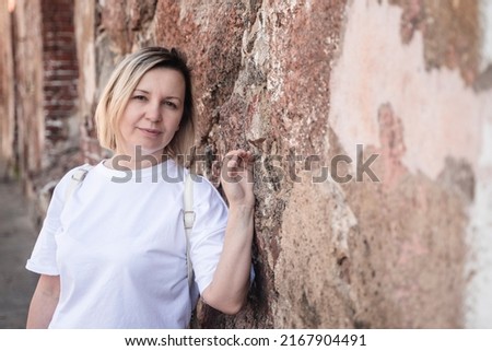 A beautiful middle-aged woman stands against an old brick wall. High quality photo